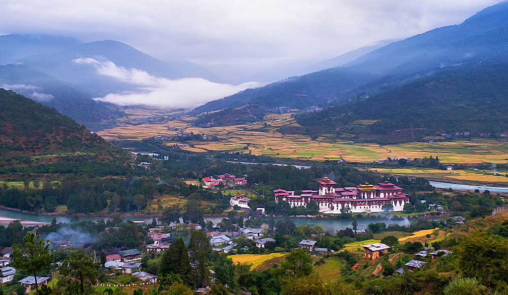 Punakha Dzong beside the river in Bhutan, with terraced fields and mist across the valley