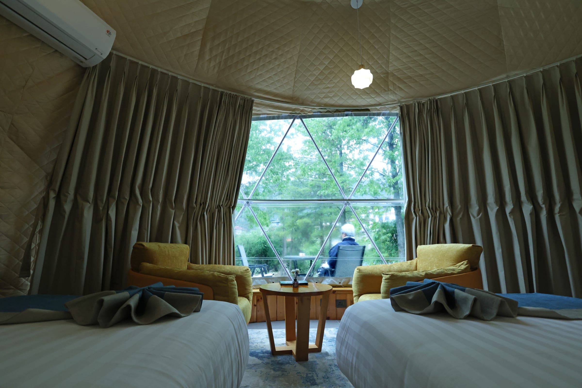 Deluxe Dome interior with twin beds and a panoramic geodesic bay window facing the pine forest at Kepdinkha, Paro