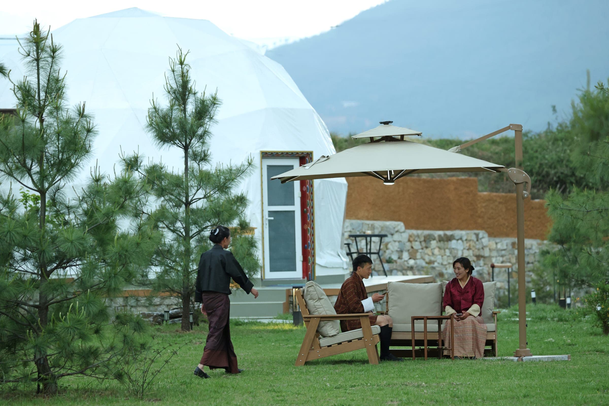 Guests relaxing on the riverfront lawn beside a glamping dome at Highland Glamping